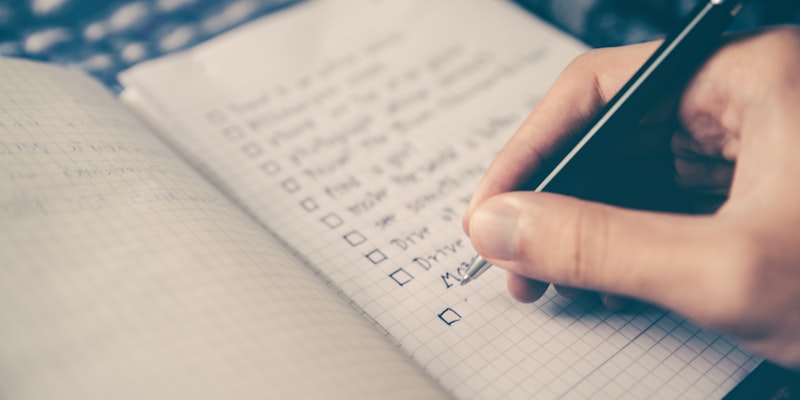 Person's hand writing a checklist in a notebook