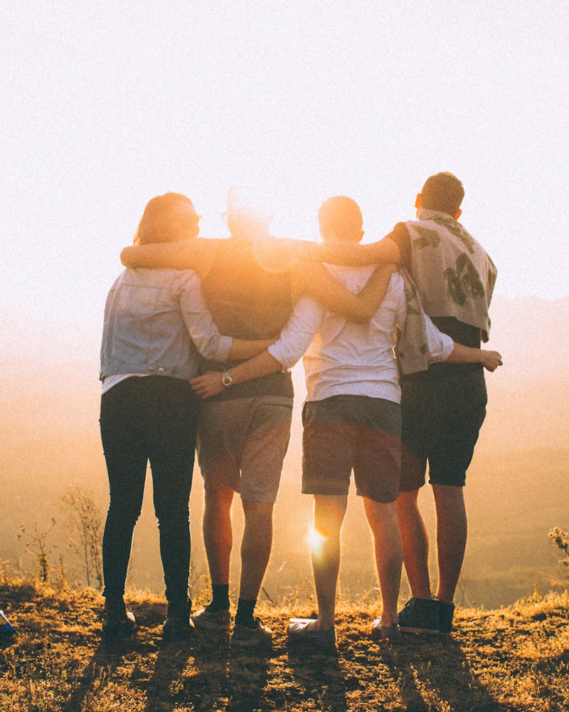 Diverse group of young friends with arms around each other at golden hour sunset