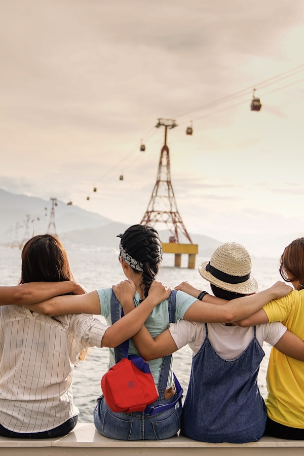 Group of teen girls sitting together with arms around each other, looking out at a scenic waterfront